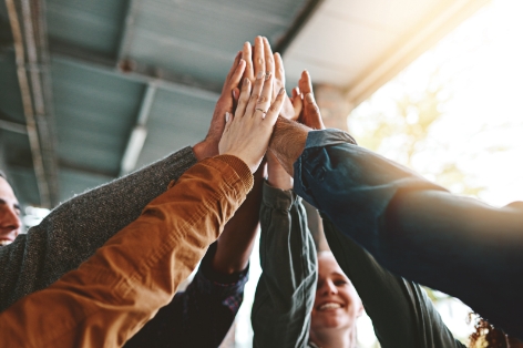 Group of hands stacked together in a high-five to celebrate teamwork and collaboration.